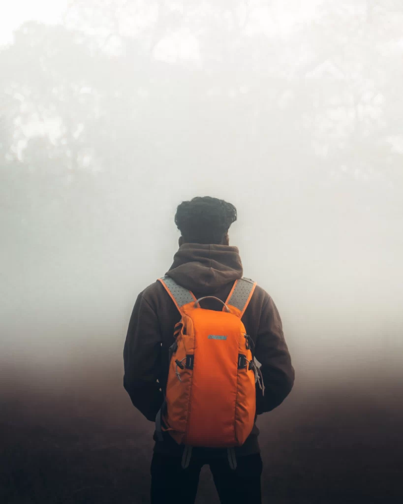 man wearing backpack looking off into the fog